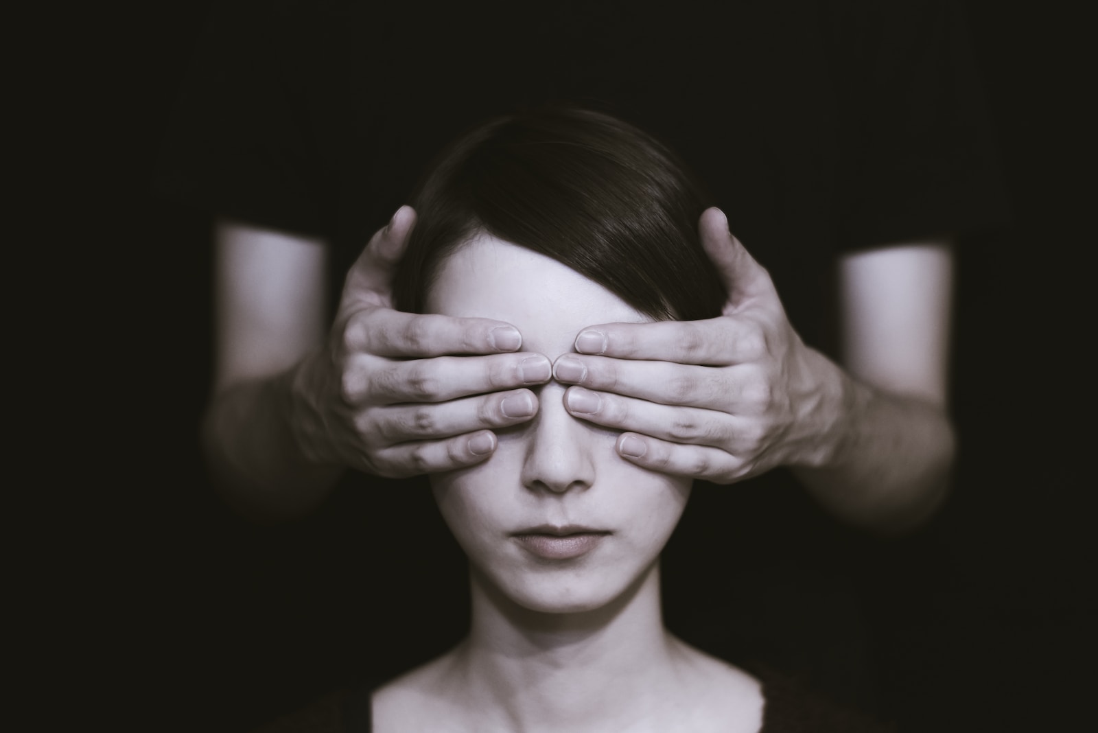 Person covering the eyes of woman on dark room