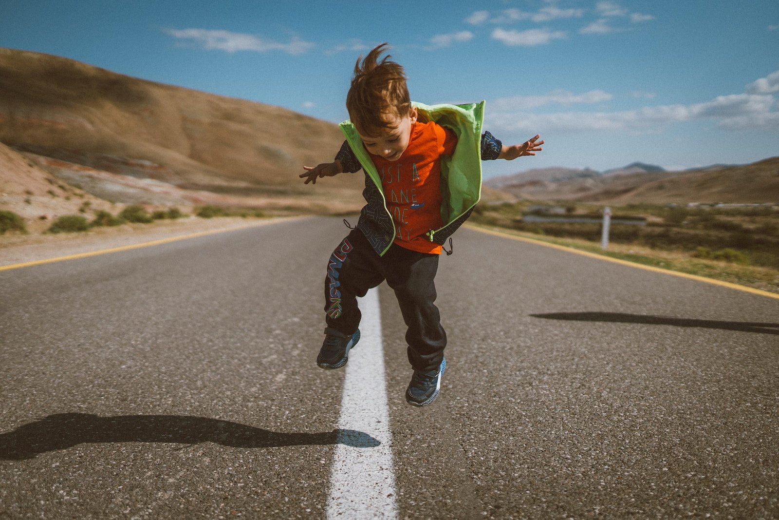 A young boy is jumping in the air on a road