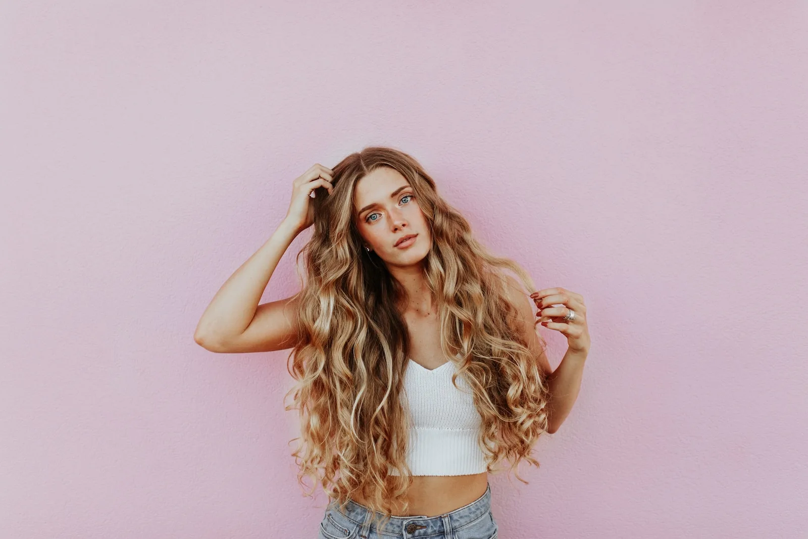 Woman standing next to pink wall while scratching her head