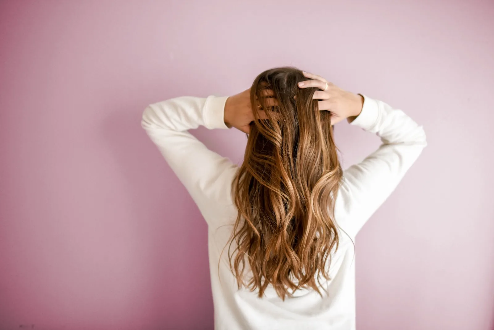 Woman in white long sleeved shirt standing in front of pink wall