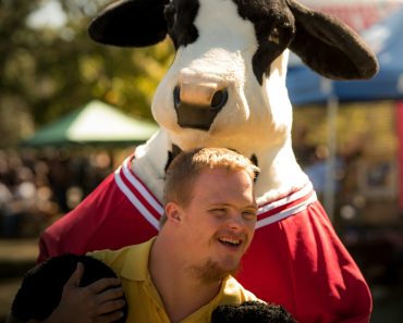 smiling man wearing yellow polo shirt standing near cattle cosplay