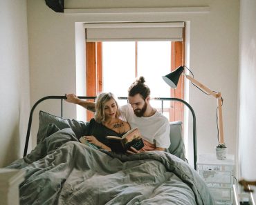 man and woman reading book on bed