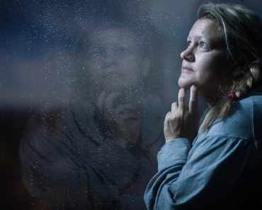 clear glass window panel casting reflection of woman touching her jaw