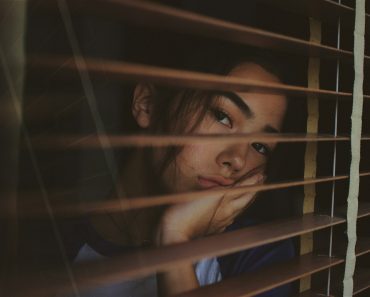 a woman looking out of a window with blinds