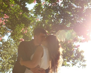 man kissing woman under green tree during daytime