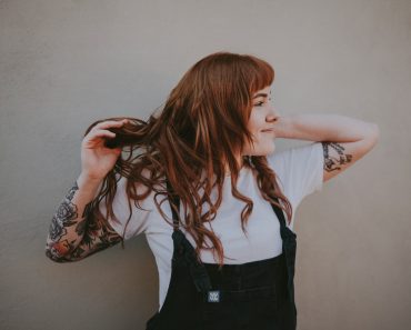 woman holding her hair standing against gray wall