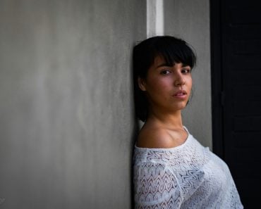 woman wearing white shirt leaning against gray wall