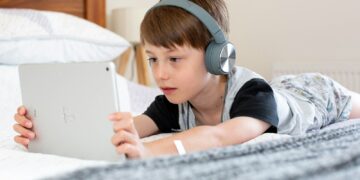 boy in blue shirt wearing headphones lying on bed