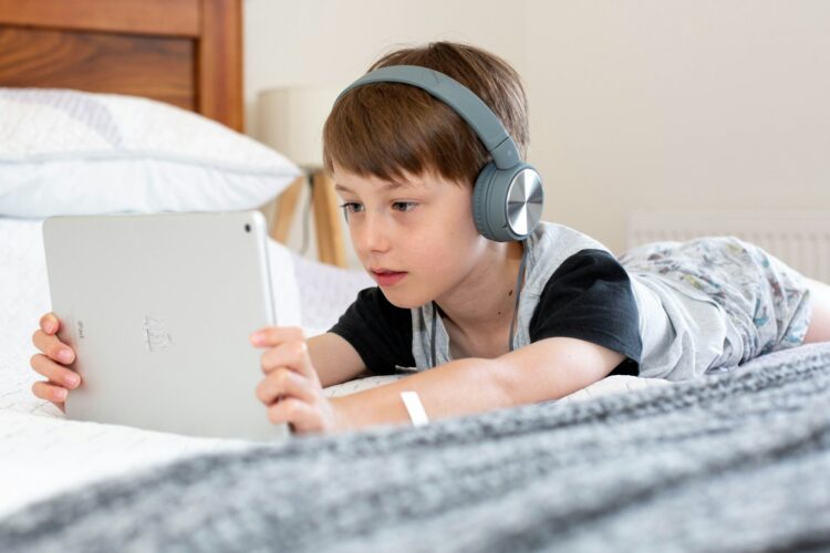 Boy in blue shirt wearing headphones lying on bed
