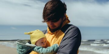 man in black jacket carrying baby in yellow hoodie