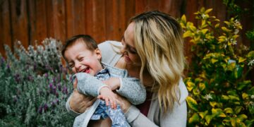 woman in gray sweater carrying baby in blue and white shirt