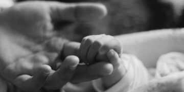 a black and white photo of a person holding a baby's hand