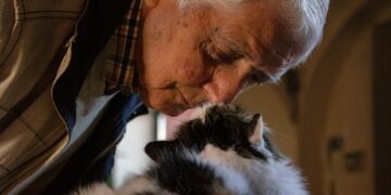 man in black and white jacket holding white and black cat