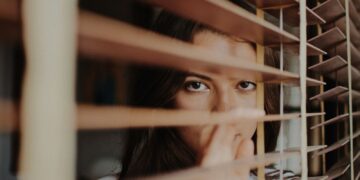 woman peeking over window blinds
