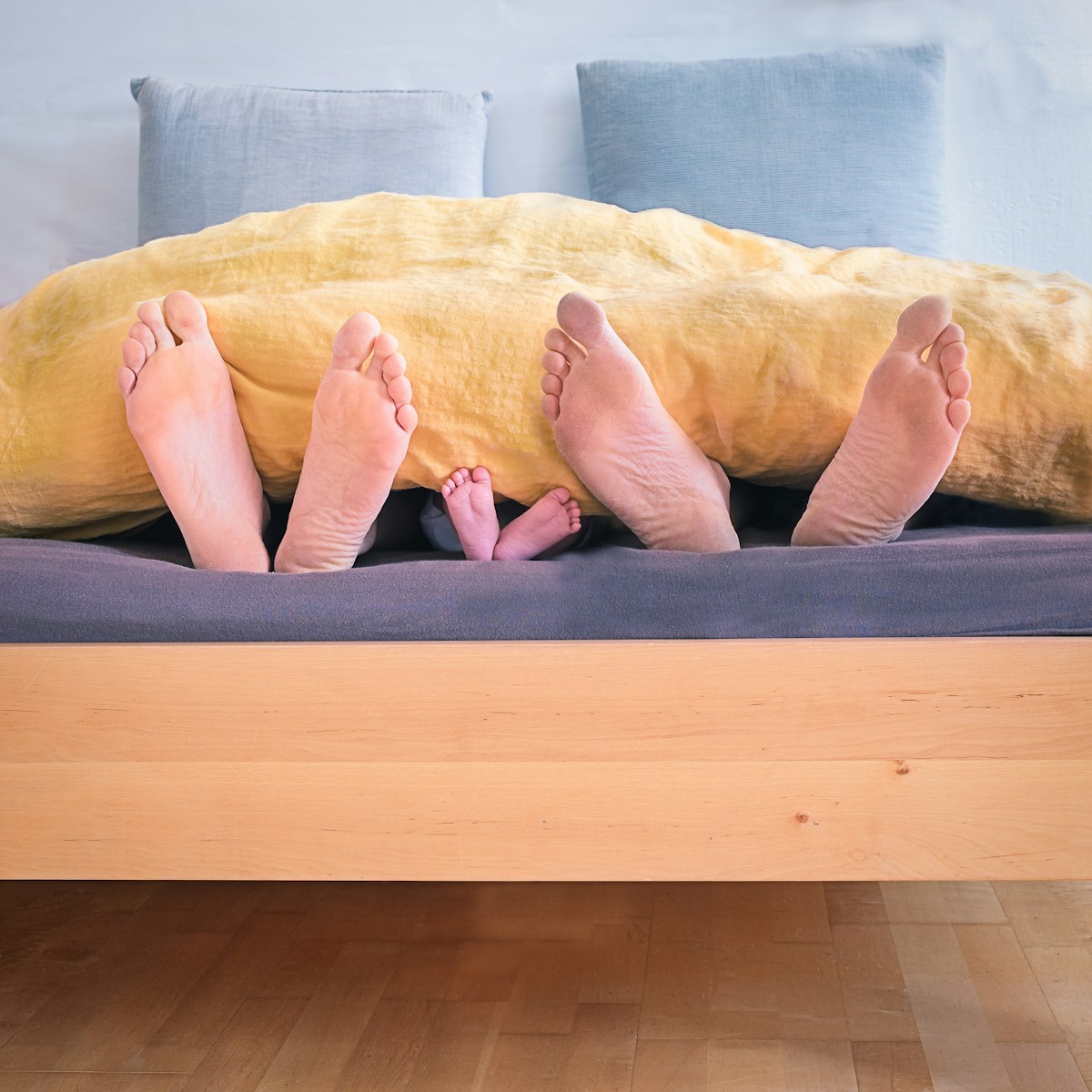 Three people underneath yellow bed blanket