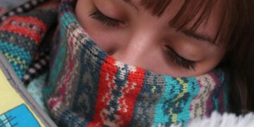 Woman resting with eyes closed, wrapped in a warm, colorful wool scarf, depicting comfort and warmth.