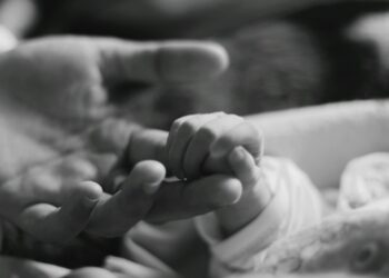 a black and white photo of a person holding a baby's hand