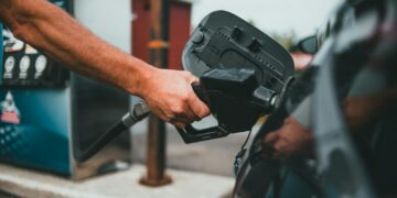 Close-up of a hand holding a nozzle while refueling a car at a gas station.