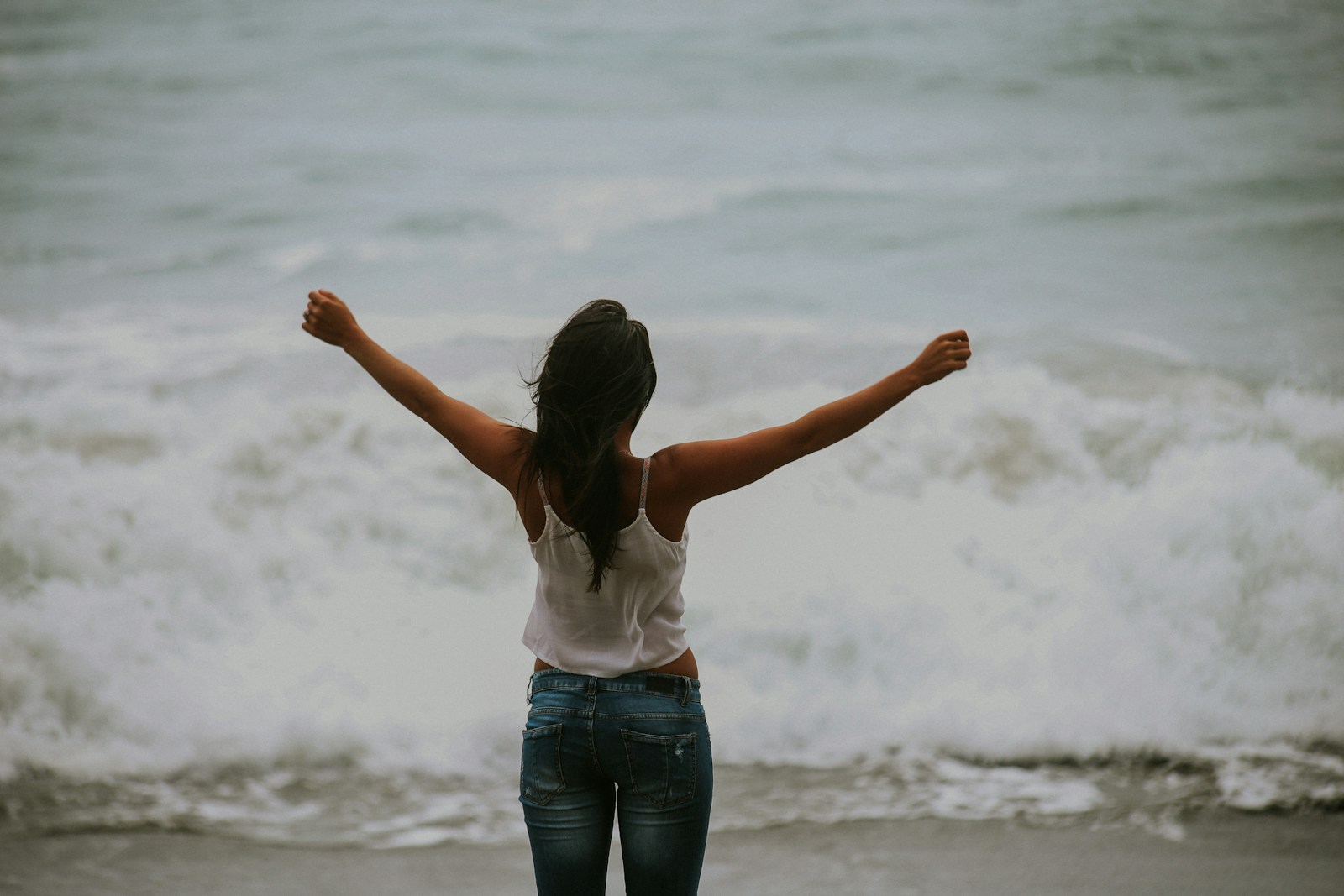 Woman in white spaghetti strap top standing on the seashore