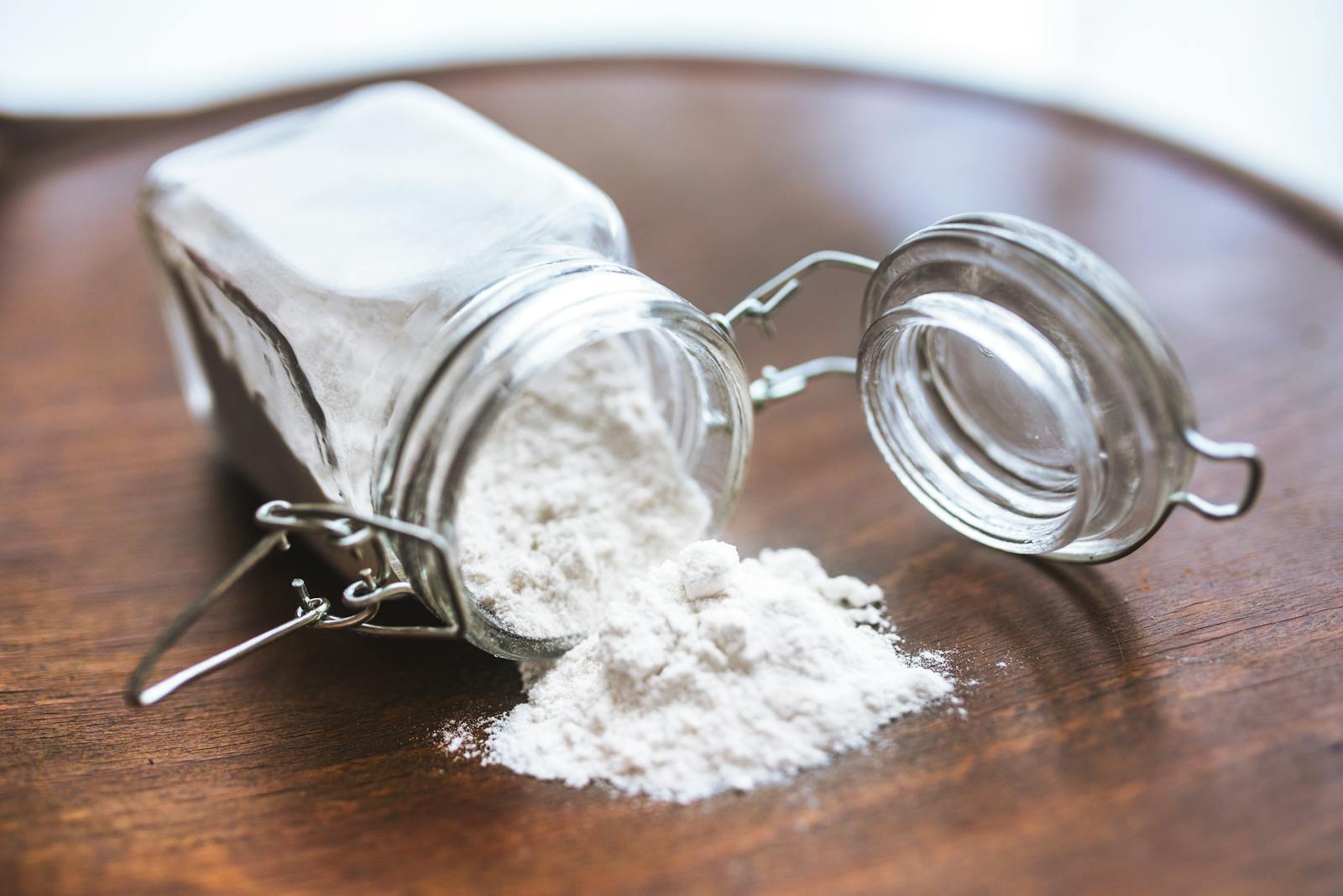 Glass jar tipped over with white flour spilling onto a wooden surface ideal for baking themes