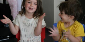 two young children sitting in chairs with their hands in the air