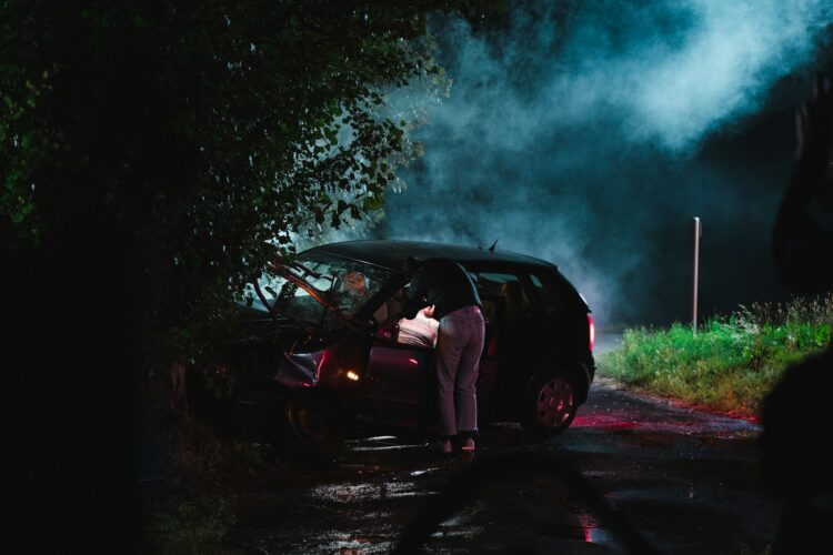 A person standing next to a car with smoke coming out of it