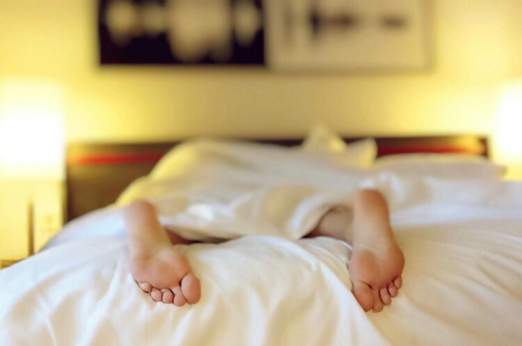 A person relaxing on a bed with feet under white sheets conveying serenity