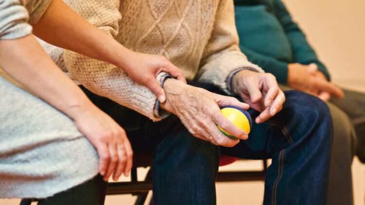 An elderly person receives support from a caregiver holding hands indoors showcasing compassion