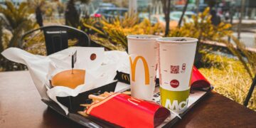 An appetizing fast food meal with burger, french fries, and drinks on an outdoor table in urban setting.
