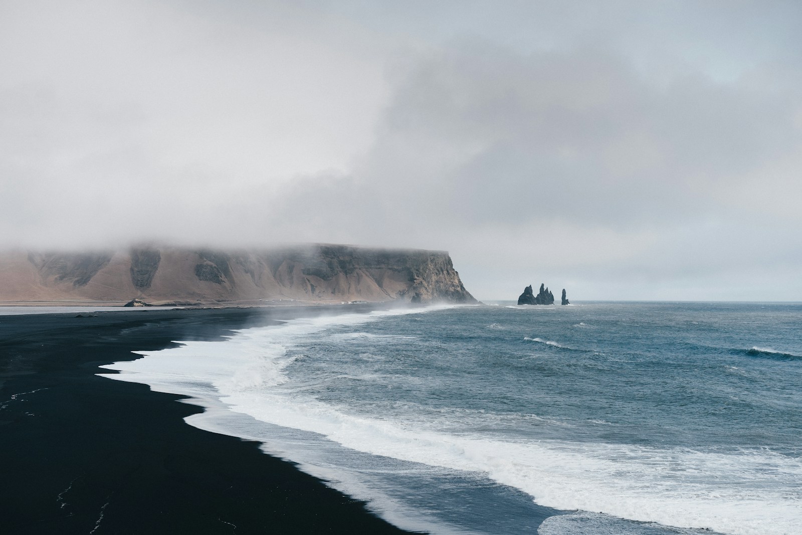 Black sand near body of water under the cloudy sky during daytime