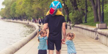 man in black t-shirt and brown shorts holding girl in blue and black jacket walking