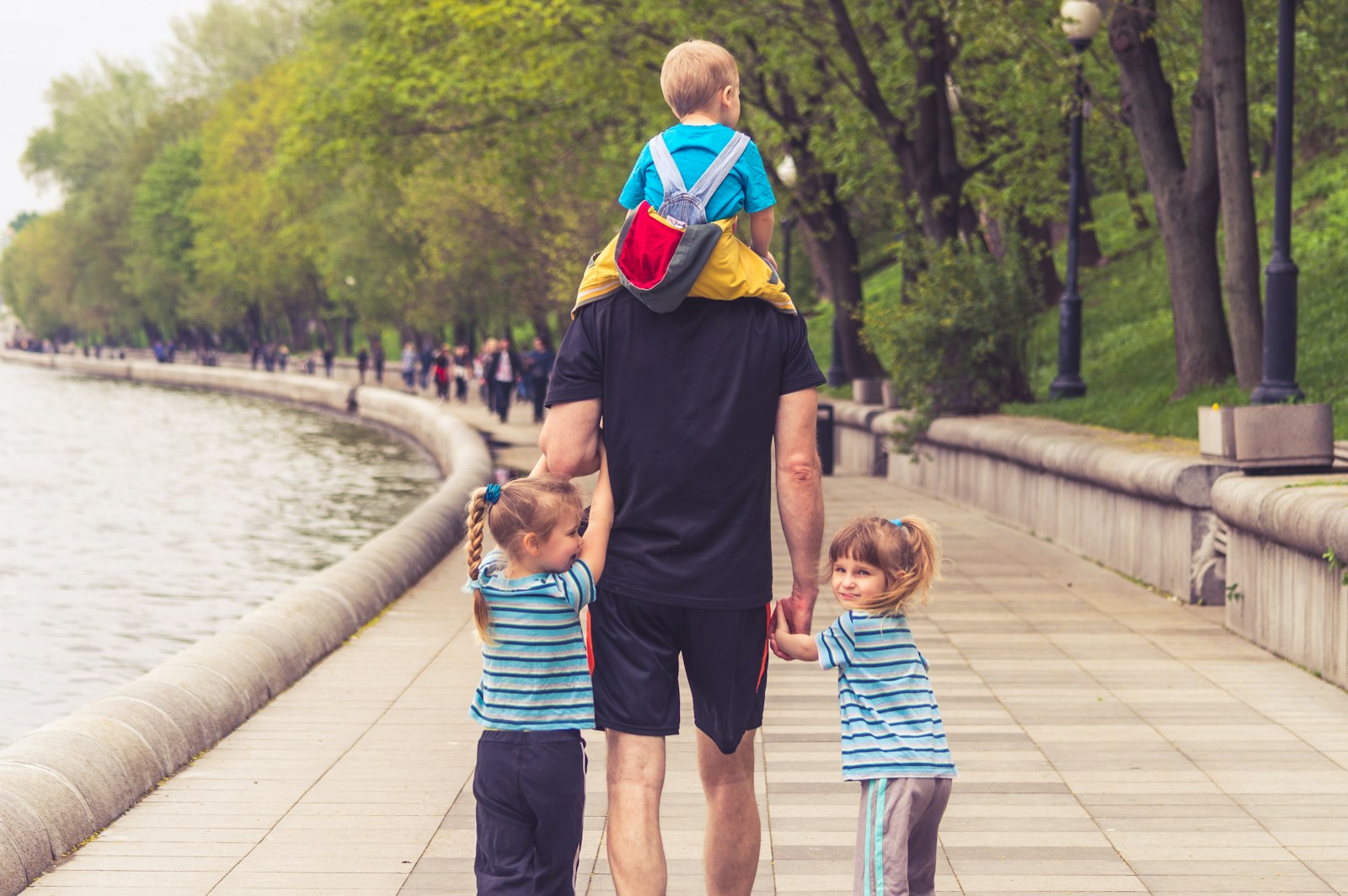 Man in black t shirt and brown shorts holding girl in blue and black jacket walking