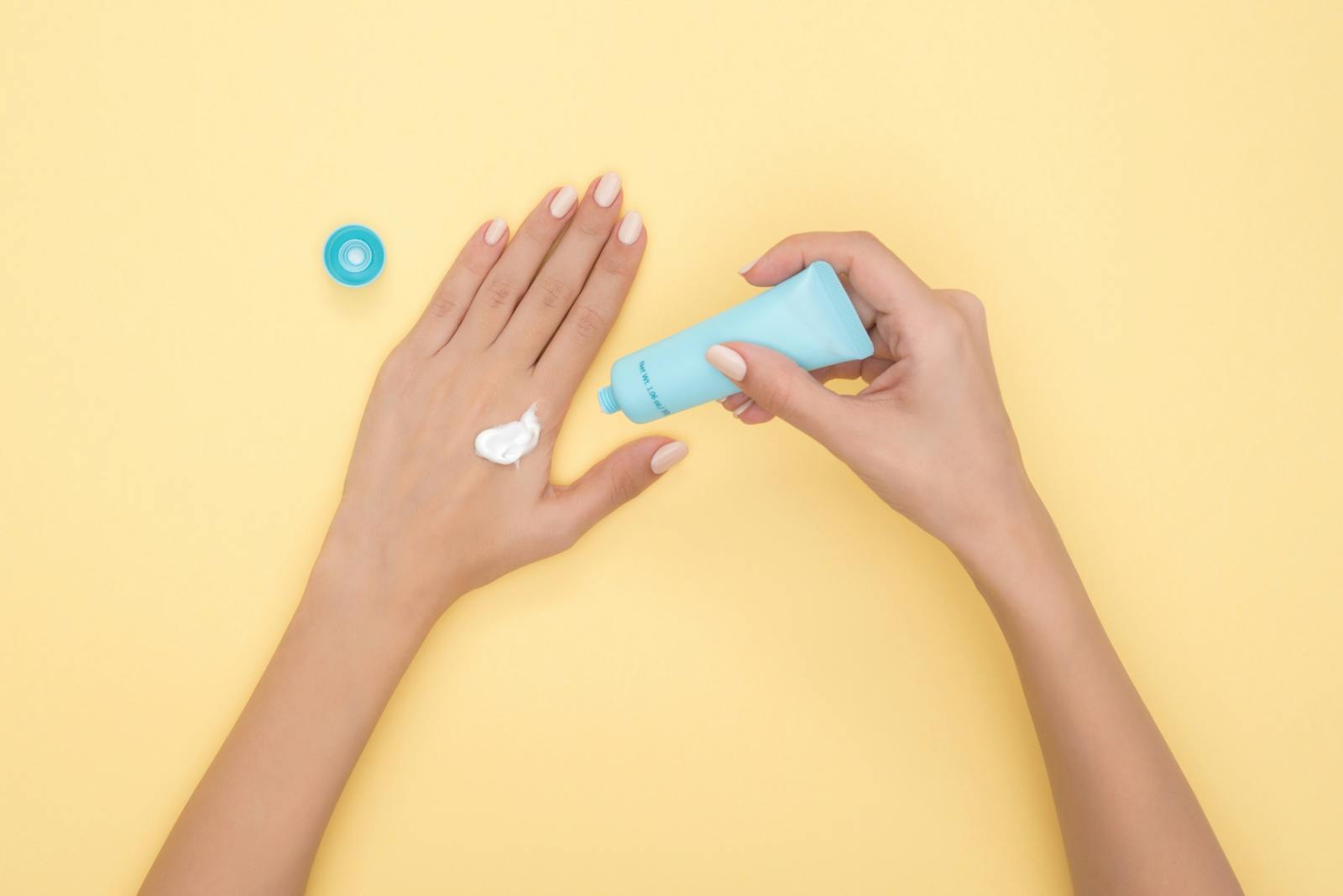 Close up of a woman's hands applying cream on a pastel yellow background. Ideal for beauty and skincare themes.