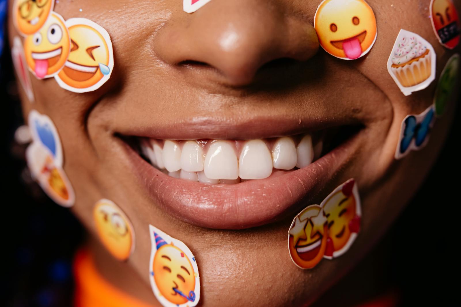 A close up of a woman's smiling face adorned with colorful emoji stickers.