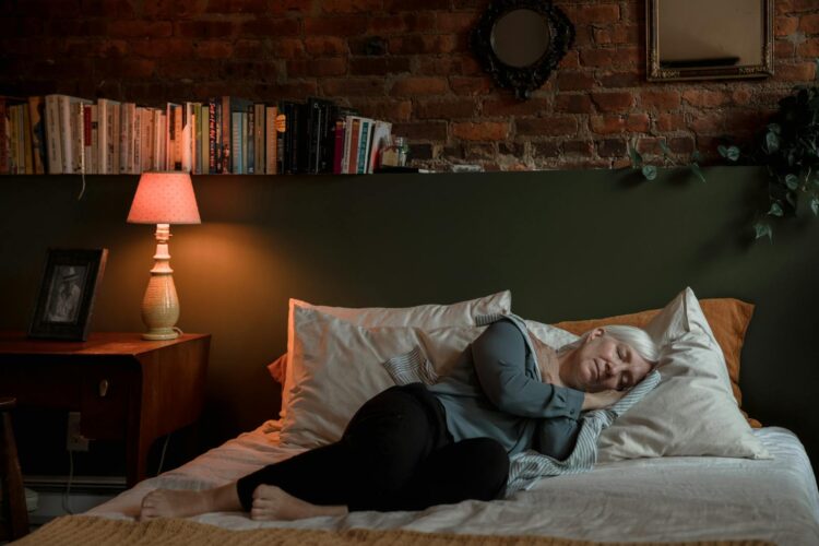 Elderly woman peacefully sleeping in a cozy bedroom with a lamp and books at night
