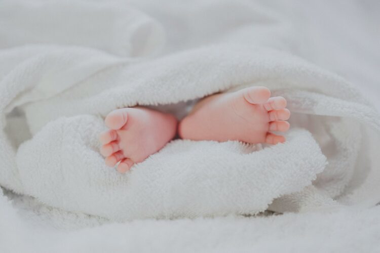 Barefooted baby covering white blanket