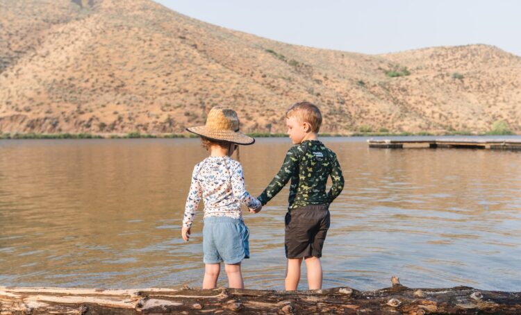 Two young boys standing on a log by the water
