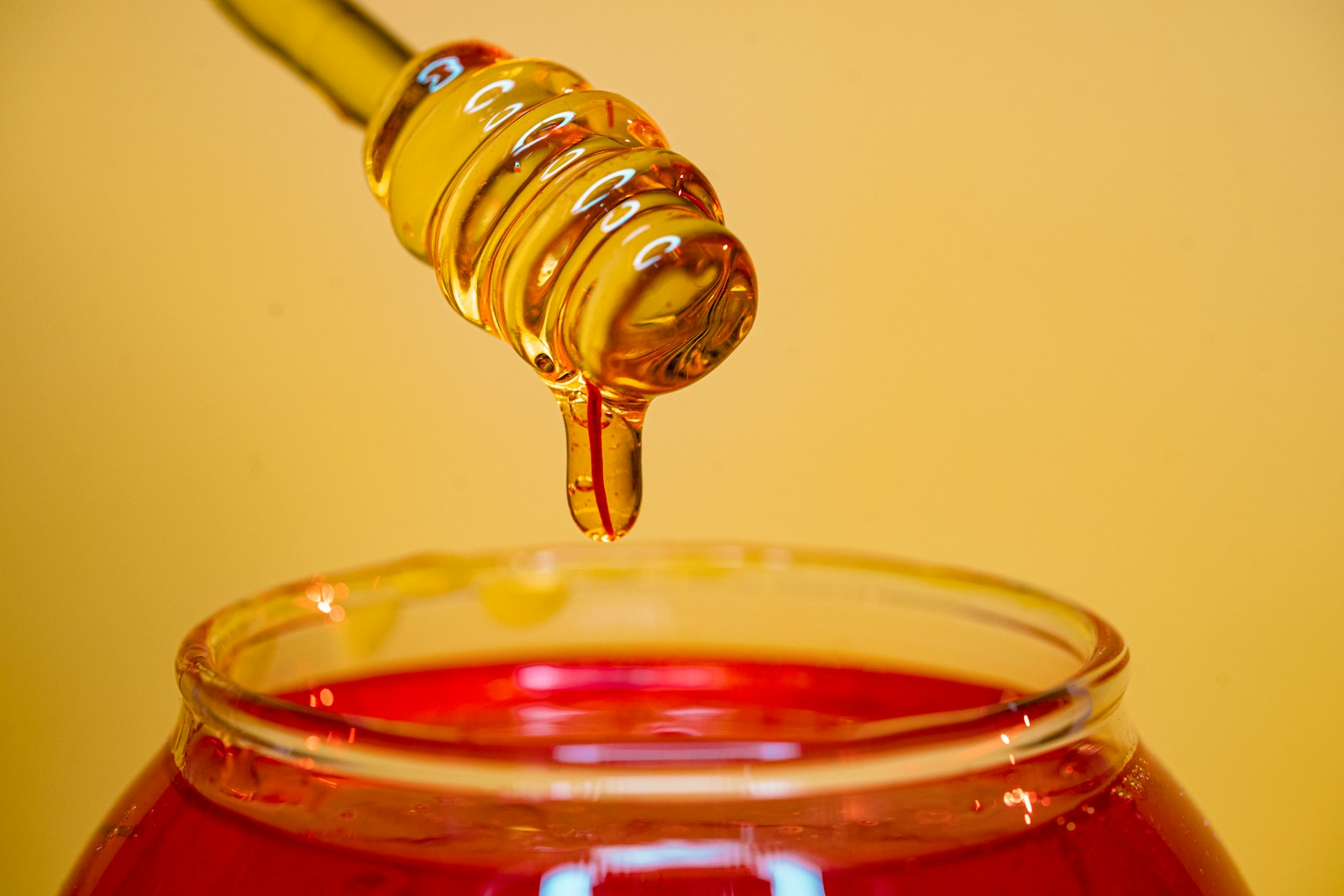 Clear glass bottle pouring red liquid on clear drinking glass