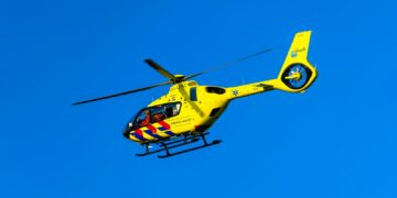 A yellow helicopter flying through a blue sky