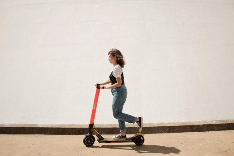 Woman in white shirt and blue denim jeans riding red and black kick scooter