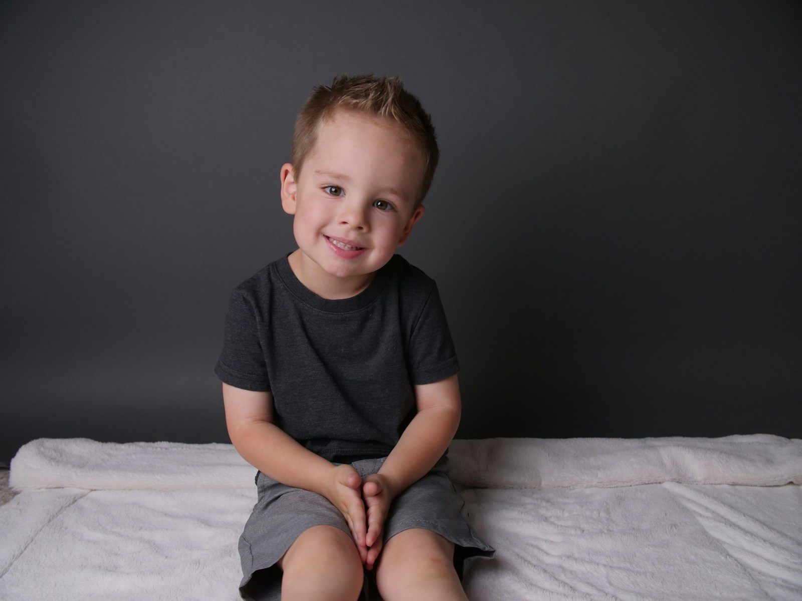 Boy in black crew neck t shirt sitting on white bed