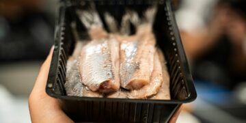person holding black plastic tray with meat