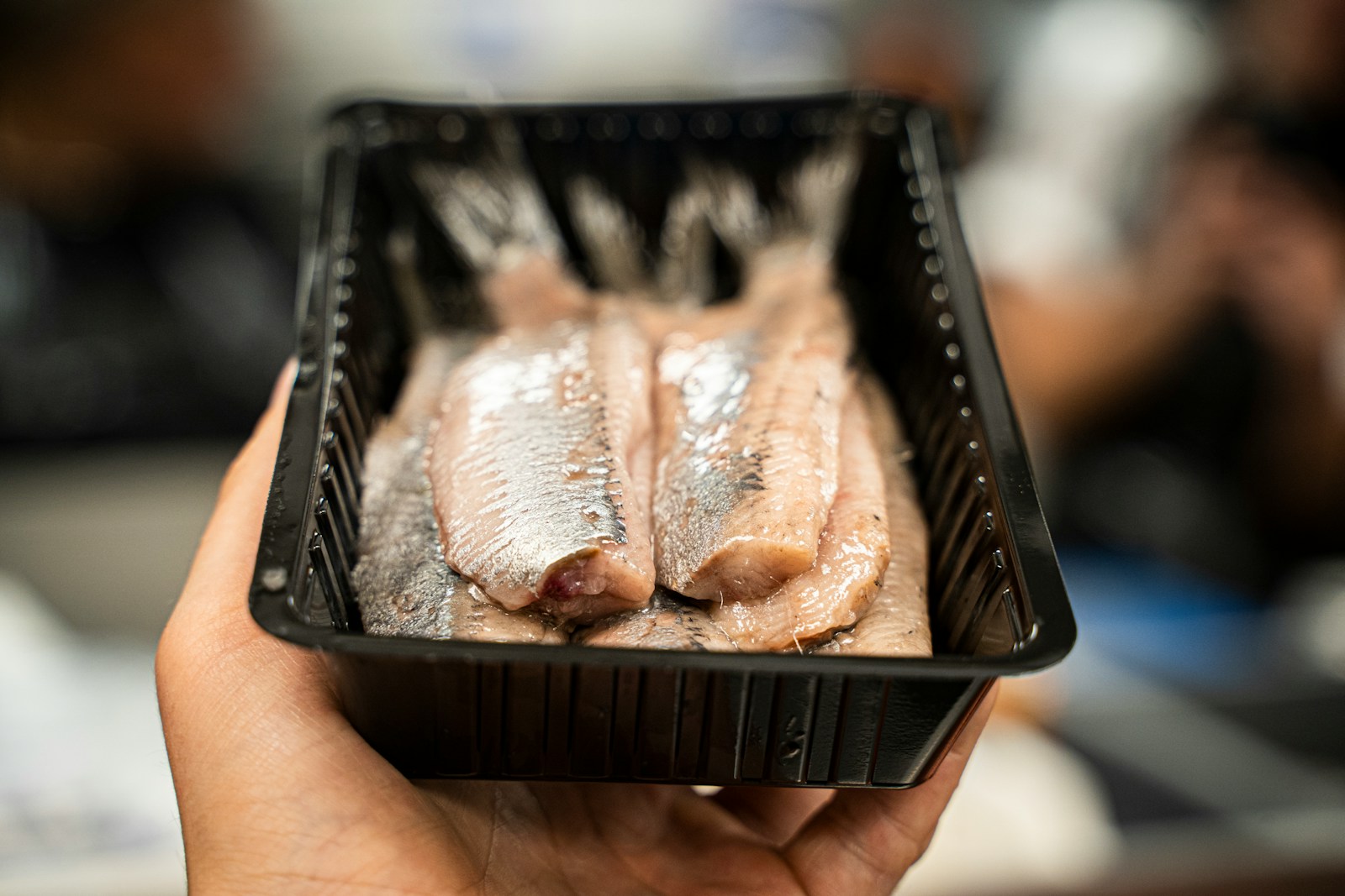 Person holding black plastic tray with meat