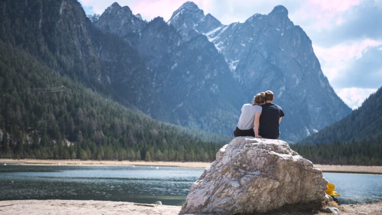 A couple sits on a rock looking out over a lake