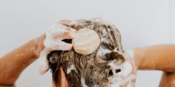 Close-up of a person washing their hair with soap bar and foam, focusing on hands and hair.