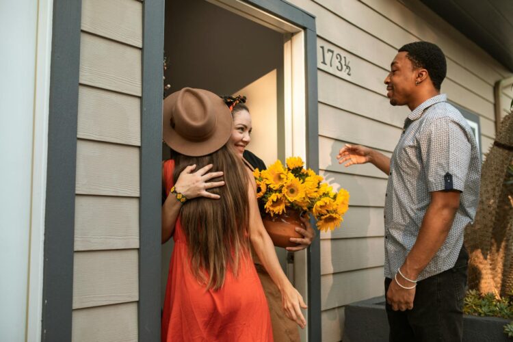 Three friends greeting and hugging at a house entrance with sunflowers