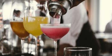 person holding cocktail shaker pouring liquid in glass during daytime