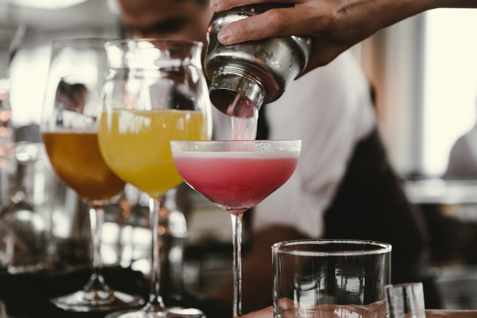 Person holding cocktail shaker pouring liquid in glass during daytime