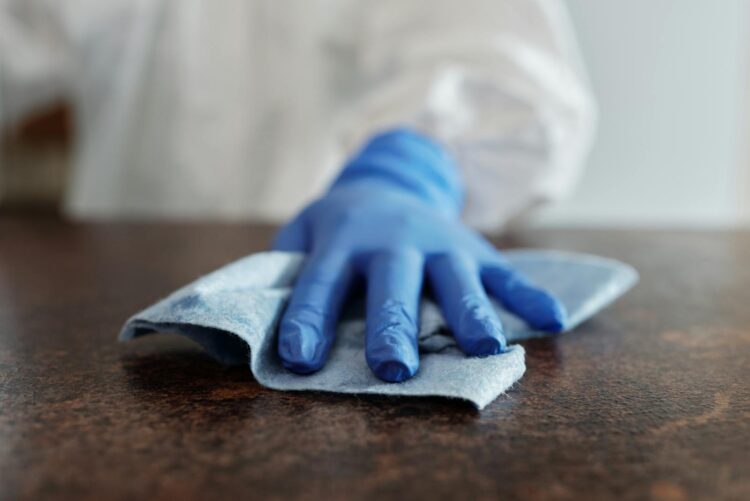 A hand wearing a blue glove wipes a surface with a cloth emphasizing hygiene and cleanliness
