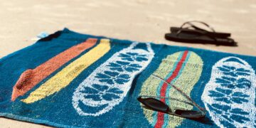 black sunglasses on blue towel beside pair of black flip-flops